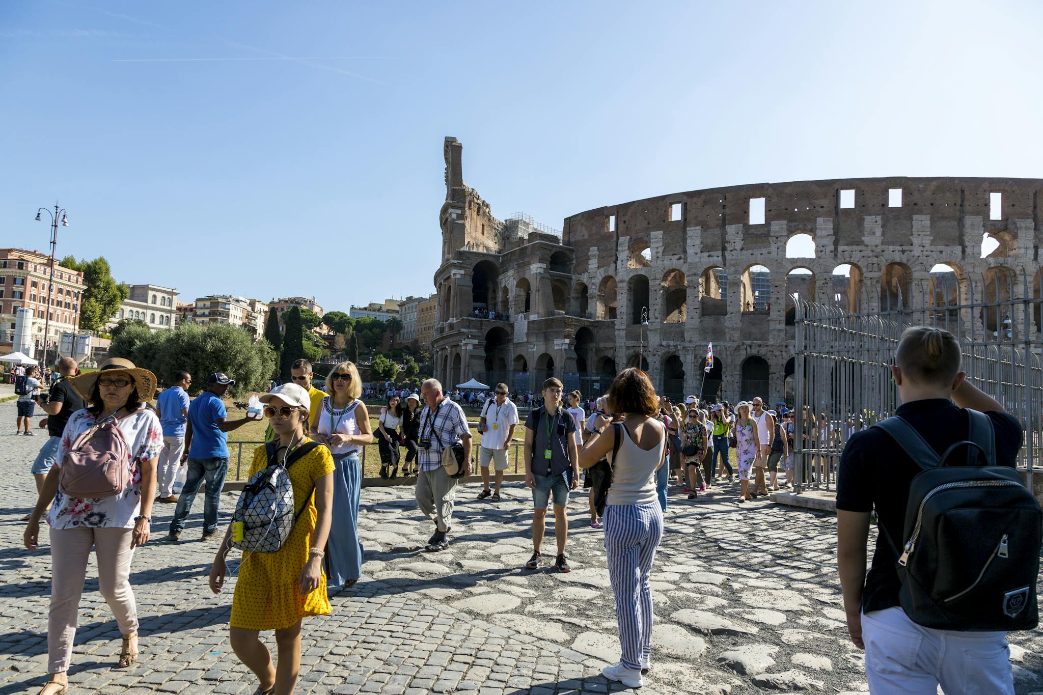 Tourists wander around the iconic Colosseum in Rome on a clear summer day, capturing memories.
